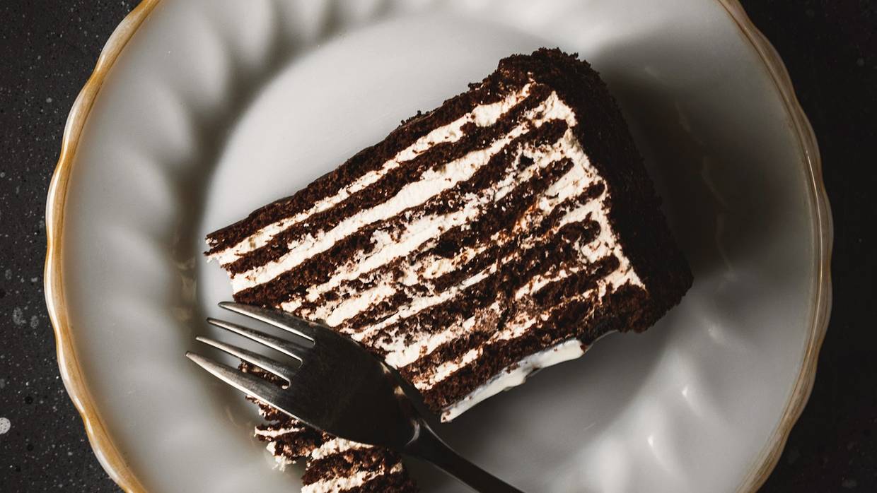 A tall slice of many-layered chocolate cake resting on a rimmed plate with a fork.
