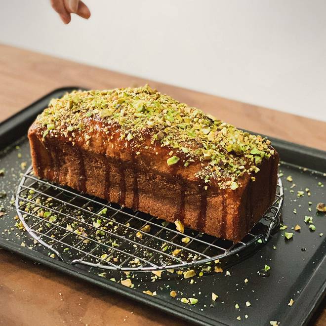 A date and tahini loaf cake on a wire rack, scattered with chopped pistachios.