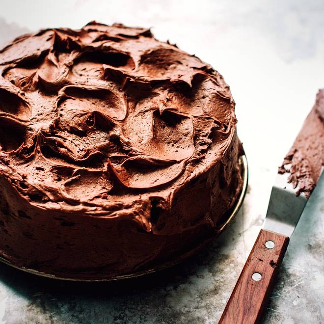 A dark chocolate cake finished in rough hand-swirled ganache, with the palette knife beside it.